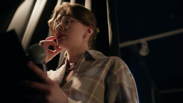Low angle shot of young adult female comedian reviewing speech script standing backstage while feeling anxious before live show