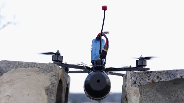 Horizontal shot of a tactical FPV kamikaze drone with a mounted explosive payload taking off from a concrete structure against a bright sky background