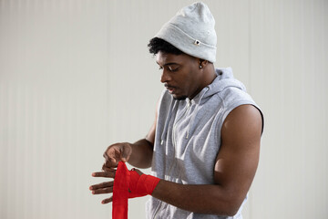 Young man concentrating, preparing for boxing training, wrapping his hands with red bandages for...