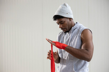 Athlete preparing for boxing workout, carefully wrapping hands with red bandages, showing focus and...