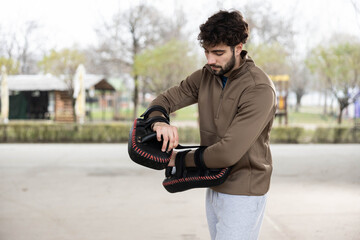 Young athletic man adjusting focus mitts and preparing for a personal martial arts or boxing...