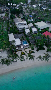 Aerial view of luxury beachfront villas with a swimming pool and palm trees along the turquoise coastline in Siargao, Philippine