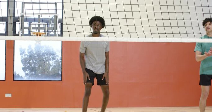 Diverse male players spiking volleyball after pass, gray tee attacker jumping at net in gym scoring