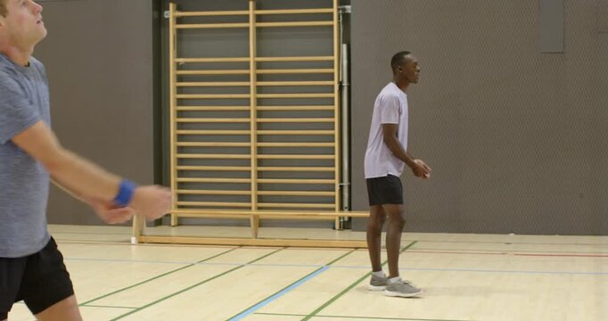 Diverse male teammates training, cradling then bumping incoming ball near net in gym, copy space