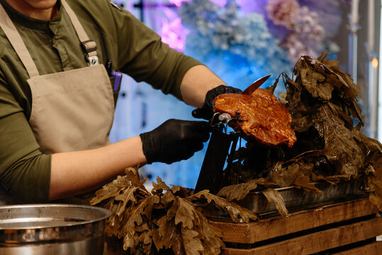 male kitchen worker prepares meat, cutting with knife as element of show in front of audience, cropped, unrecognizable