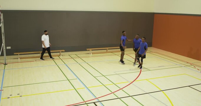 Blue-shirted males moving in gym as ball rolling, huddling with coach checking spots, copy space