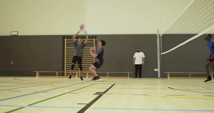 Men's volleyball teams rallying at school gym, blue attacker spiking net to score, blocker jumping