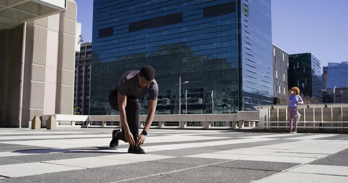 Adult African American man tying shoe on rooftop plaza, noticing lace to resume jogging, copy space