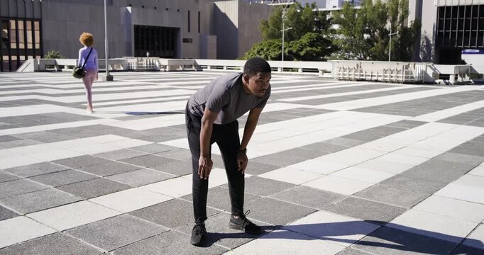 African American man bending breathing hard standing checking wristwatch walking plaza in grey tee