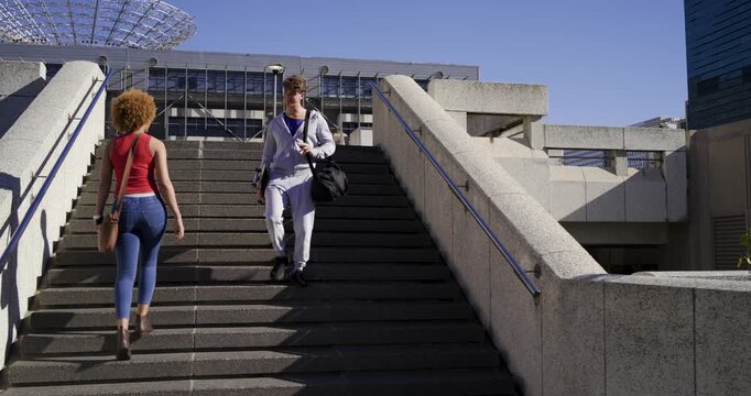 Pair nearing plaza steps woman climbing phone man descending skateboard bag camera following moving