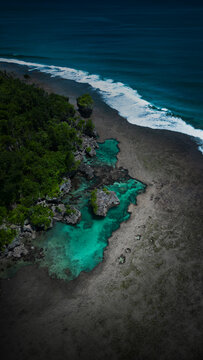 Aerial view of turquoise rock pools along a rugged coastline with lush green trees and crashing ocean waves Magpupungko pool, Ph