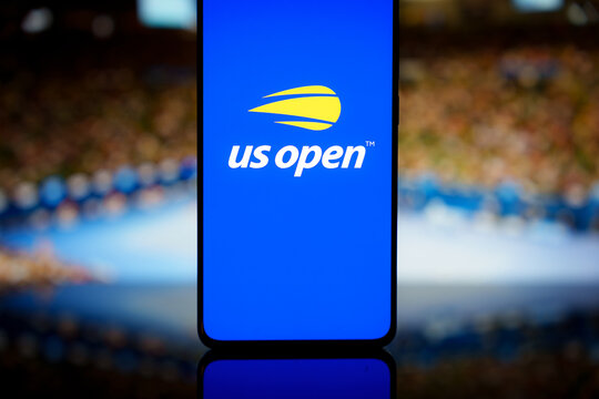 US Open tennis logo displayed on a smartphone screen with a blurred stadium background, representing mobile sports broadcasting and grand slam tournament app coverage
