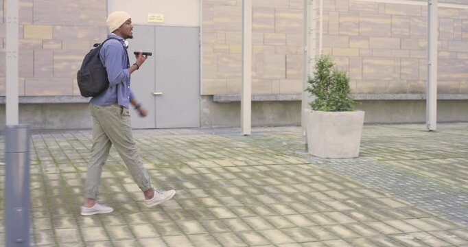 After call, African American man crossing plaza, sitting on planter and speaking into smartphone