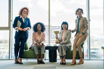 Fototapeta premium Empowered businesswomen team celebrating success holding a golden trophy