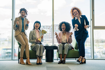 Fototapeta premium Empowered businesswomen team celebrating success holding a golden trophy