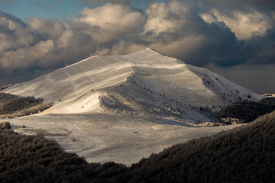 Breathtaking winter view of Smerek peak in Bieszczady Mountains with hikers on a snowy trail under dramatic golden hour sky.