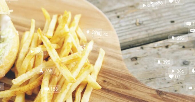 Vertical video: Showing social icons causing burger slide onto board on patio with fries for likes