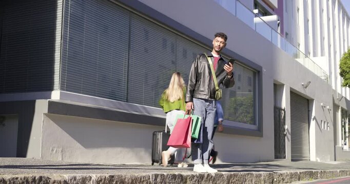 African American man on curb checking phone holding bags raising it signaling passersby moving