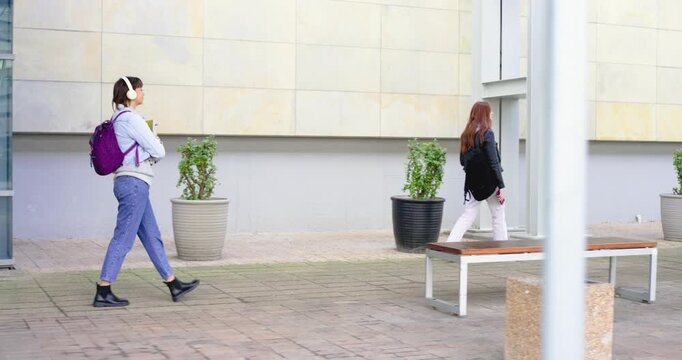 Two women commuting across plaza, redhead leading, younger entering left following checking phone