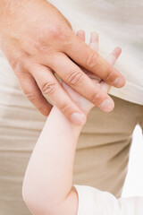 Fototapeta premium Close-up of an adult hand gently holding a child's hand, symbolizing care, protection, and connection. This intimate moment highlights a nurturing relationship and trust.