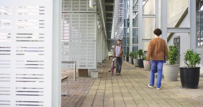 Diverse men passing, Asian pushing bicycle from far along arcade, commuting, other holding notebook