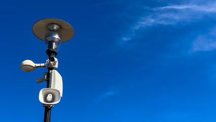 Speaker system on a pole near clear sky. A speaker system is mounted on a pole under a clear blue...