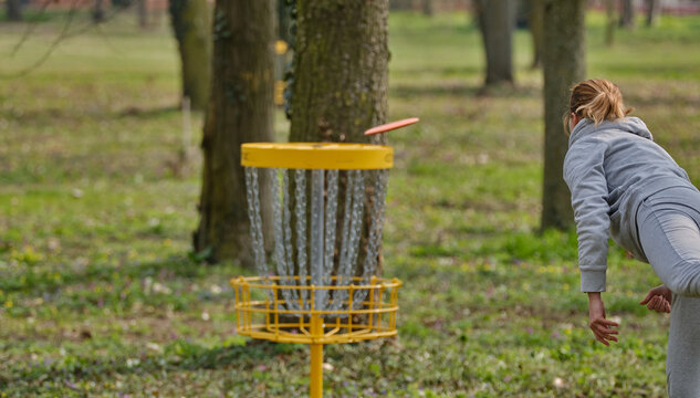 Discgolf basket with female player throwing a final shot