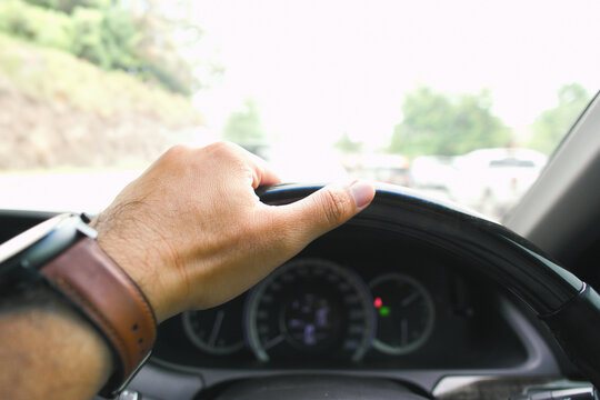 Car driving on the road, A close-up view of a driver's hand on a leather steering wheel, wearing a brown leather watch, with the car dashboard in the background.