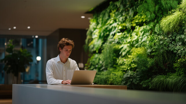Knowledge worker packing laptop bag while ignoring email about assigned desk seating in contemporary office lobby with living plant wall, perfect for remote work advocacy, office attendance, and mod