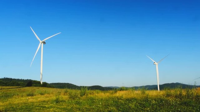 Wind generators produce clean electric power in field under clear sky. Windmills transform renewable energy into electricity at summer countryside