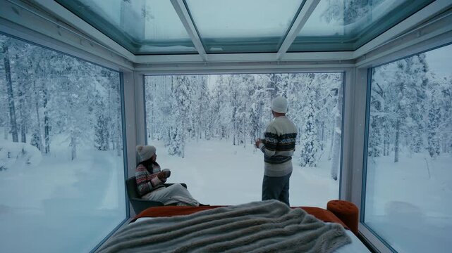 Enjoy a warm atmosphere as a couple relaxes in a glass cabin surrounded by the stunning snowy wilderness of Akaslompolo in Lapland, Finland, creating unforgettable memories together.