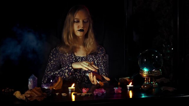 Woman psychic presents the Sun tarot card during a divination ritual with crystal ball candles smoke amethyst and runes in a dark mystical esoteric space