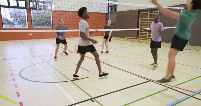Adult male gray shirt walking back at school gym after ball sent over net, catching breath