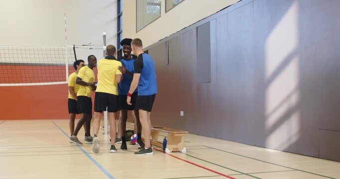 Opposing male teams in yellow blue shirts approaching net in gym postgame greeting passing ball