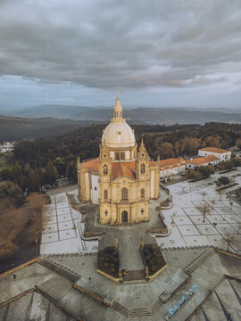 Aerial view of the Santuario de Nossa Senhora do Sameiro standing majestically against a backdrop of distant mountains, its pale dome contrasting with the dark trees, Braga, Braga, Portugal.