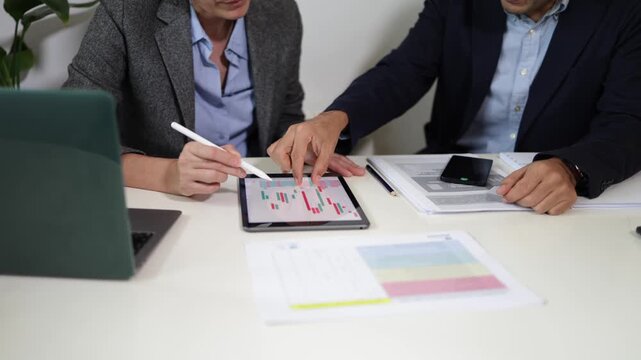 Professional business team analyzing stock market data on a digital tablet with a stylus, collaborating on investment strategy and discussing financial trends in the office