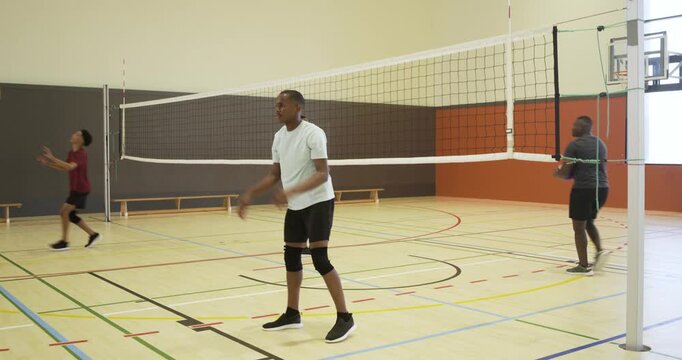 Diverse men in sportswear moving to flying volleyball, bumping, keeping rally by net, copy space