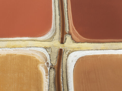 Aerial view of geometric salt ponds painted in earthy hues of ochre, terracotta, and cream, creating a striking mosaic from above, Sanlucar de Barrameda, Andalusia, Spain.