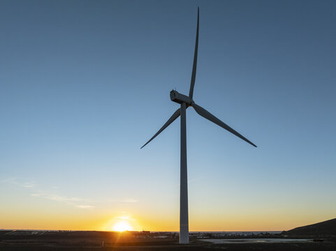 Aerial view of a wind turbine standing tall against a backdrop of a sunset, its blades reaching for the sky, Zahara de los Atunes, Andalusia, Spain.