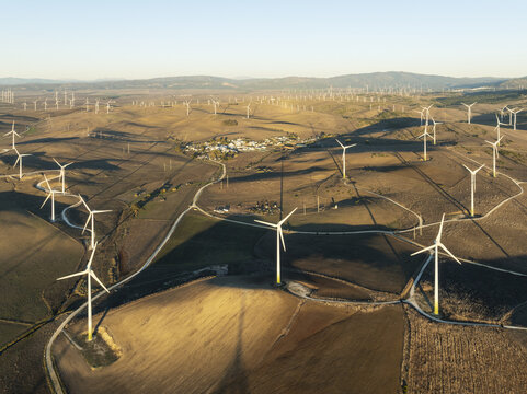 Aerial view of wind turbines standing tall across the arid landscape, casting long shadows in the golden light, Zahara de los Atunes, Andalusia, Spain.