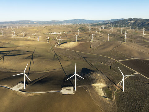 Aerial view of numerous wind turbines standing tall across the arid landscape, their stark white blades contrasting with the dry, golden earth, Zahara de los Atunes, Andalusia, Spain.