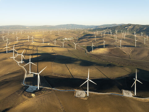 Aerial view of wind turbines standing tall against the sun-kissed hills, a symphony of white against the earthy landscape, Zahara de los Atunes, Andalusia, Spain.