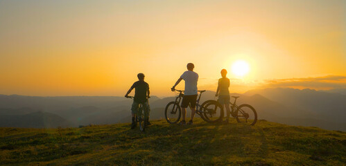 Obraz premium LENS FLARE: Group of fit tourists on bicycles observes the golden sunrise.