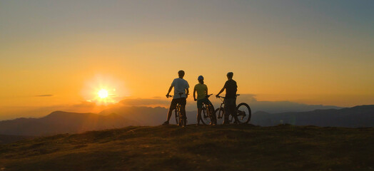 Fototapeta premium DRONE: Mountain bikers stop and observe the sunset after a downhill adventure.