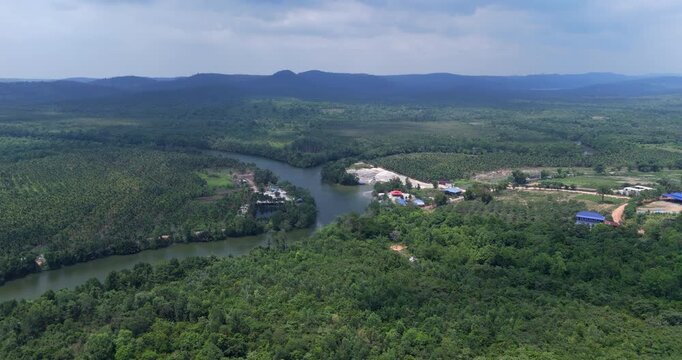 Wide forward aerial view of a winding river revealing a sand dredging site, palm plantations, and distant hills.