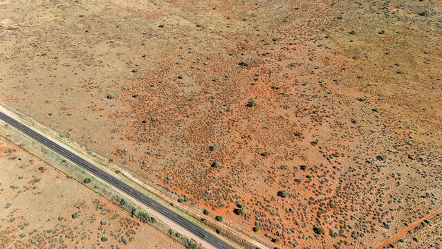 Aerial view of a stark, sun-baked landscape, where ochre earth meets a ribbon of asphalt, punctuated by sparse, resilient vegetation, Karoo Desert, Northern Cape, South Africa.