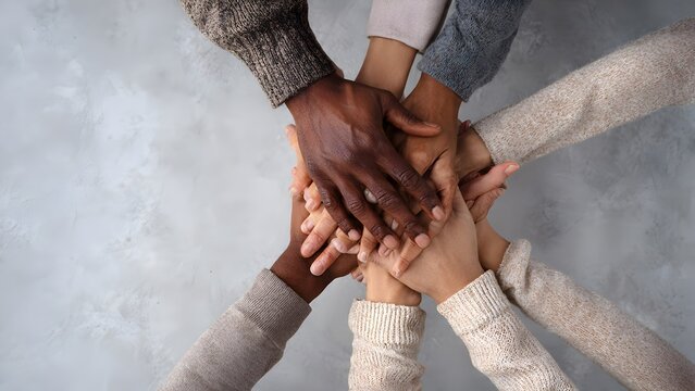 Overhead circle of many diverse hands in muted business casual tones representing equality and shared ambition