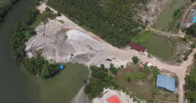Tilting down top down aerial of a sand dredging operation revealing a pump barge and heavy machinery by a lush forest.