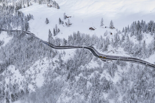 Aerial view of a winding road cutting through a snow-blanketed landscape, with scattered chalets nestled among the trees, Ormont-Dessus, Switzerland.
