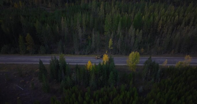 Aerial drone tracking heavy equipment machinery driving on road running through dense forest in northwest Montana